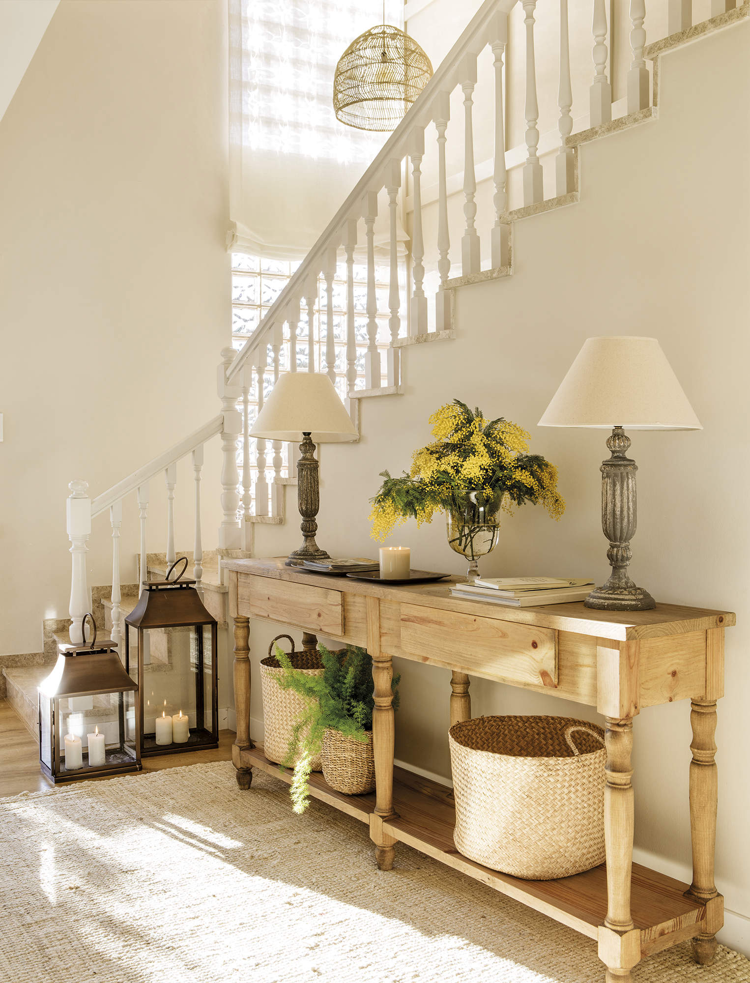 Recibidor con mueble de madera, lámparas portátiles, lámparas de mesa con pantalla de tela, flores amarillas, escalera blanca.